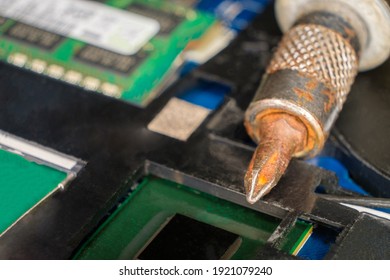 Technology craftsmanship: close-up macro view of disassembled electronic gadget reveals intricate circuitry details on memory modules and metallic motherboard with precision screwdriver. This tool features rusted tip suggesting extensive use, adding authentic repair atmosphere to technical workshop environment. Green and black components including RAM modules with bright connectors contrast sharply against dark backdrop, evoking sense of engineering richness. Soft diffused lighting enhances textures of hardware surfaces, creating focused technical mood suitable for DIY maintenance tutorials. Image captures delicacy required in electronics work with depth of field keeping screwdriver and board in clear focus while slightly blurring backgrounds. Color scheme of dark tones punctuated by vibrant greens makes this ideal for educational content about computer hardware upgrades.
