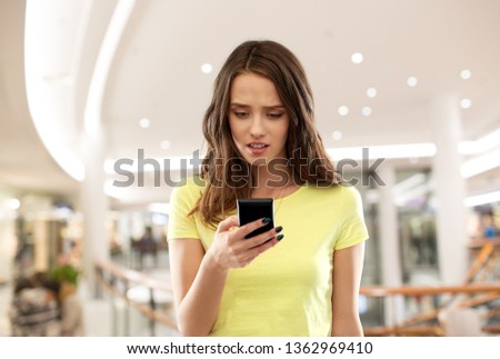 technology, cyberbullying and people concept - young woman or teenage girl in blank yellow t-shirt using smartphone over mall background