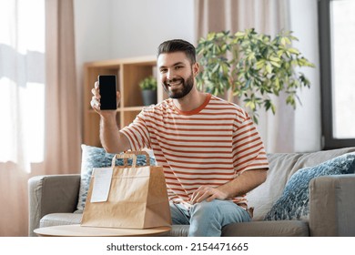 Technology, Delivery And People Concept - Smiling Man With Smartphone And Takeaway Food In Paper Bag At Home