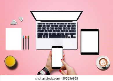 Technology Devices On Pink Background, View From Above. Office Equipment Placed Beside Laptop And Tablet. Woman Holding Phone In Hand And Touching Screen With Finger