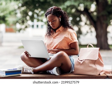 Technology, Education And People Concept - African American Student Girl In Earphones With Laptop Computer And Books In City