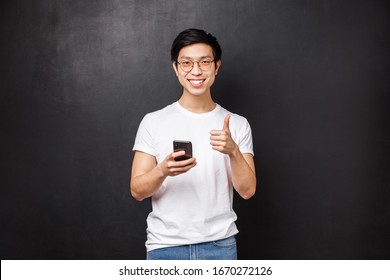 Technology, Gadgets And People Concept. Satisfied Handsome Asian Guy Using Mobile Phone Application, Delivery Service Or Internet Store, Show Thumb-up As Approve And Recommend App