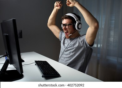 Technology, Gaming, Entertainment, Let's Play And People Concept - Happy Young Man In Eyeglasses With Headset Playing And Winning Computer Game At Home And Streaming Playthrough Or Walkthrough Video