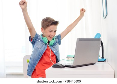 technology, gaming and people concept - boy with headphones playing video game on laptop computer and celebrating victory at home