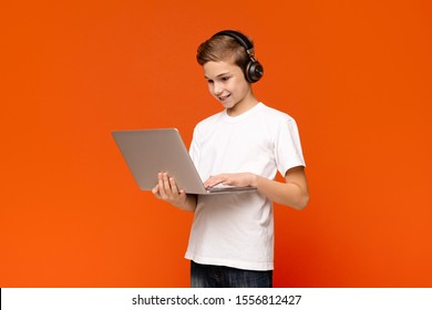 Technology, gaming and teens concept. Teenage boy in headphones playing video game on laptop computer, orange background