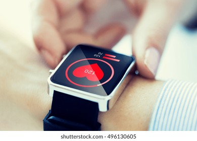 technology, health care and people concept - close up of woman hands checking pulse by smartwatch with heart icon on screen