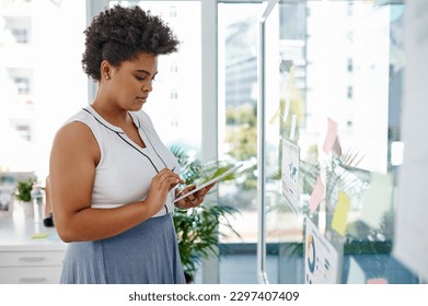 Technology helps elevate her ideas a little more. a young businesswoman using a digital tablet while brainstorming with notes on a glass wall in an office.