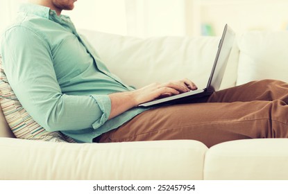 Technology, Home And Lifestyle Concept - Close Up Of Man Working With Laptop Computer And Sitting On Sofa At Home