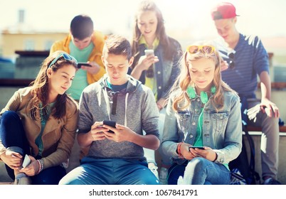 technology, internet addiction and people concept - happy teenage friends with smartphones outdoors - Shutterstock ID 1067841791