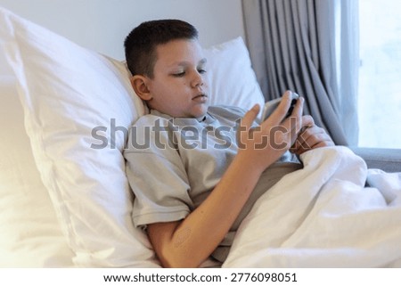  Technology and internet concept. Boy laying on bed and looking at smartphone. Child playing with mobile phone, lying on a bed. Freetime.