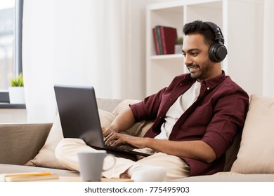 technology, leisure and people concept - happy man in wireless headphones with laptop computer listening to music at home