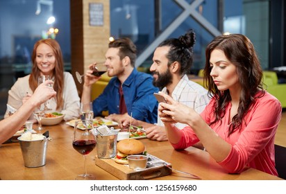 technology, lifestyle and people concept - bored woman dining with friends and messaging on smartphone at restaurant - Powered by Shutterstock