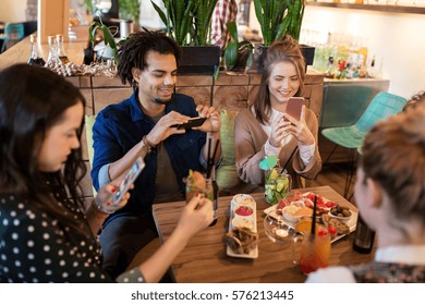 Technology, Lifestyle And People Concept - Happy Friends With Smartphones Taking Picture Of Food At Restaurant