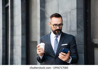 Technology Lifestyle Smart Successful Businessman Hands Holding Smartphone Coffee Cup Outdoor , Online Meeting. Portrait Professional Caucasian People Man Manager Wearing Suit Work Outdoors.  