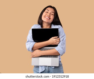 Technology Lover Concept. Happy Asian Woman Hugging Laptop With Black Blank Empty Screen, Holding It Tight Near Chest. Casual Female Geek Posing Isolated Over Studio Background Wall, Copy Space