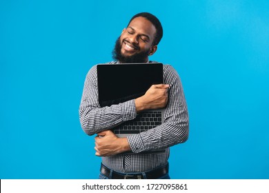 Technology Lover Concept. Happy black man hugging laptop with blank screen, isolated over blue studio wall