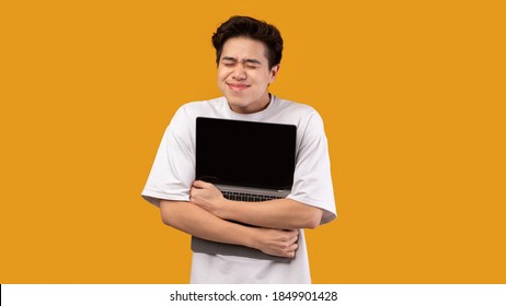 Technology Lover Concept. Happy excited asian man hugging laptop with black blank empty screen, holding it tight near chest. Geek posing isolated over orange studio background wall, copy space - Powered by Shutterstock