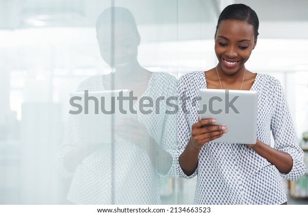 Technology\
makes work a pleasure. Shot of a young woman leaning against a\
glass divider while using a digital\
tablet.