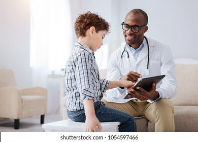 Technology in medicine. Positive pleasant male doctor smiling while showing tablet to boy and sitting