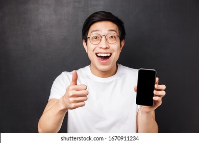 Technology, Messaging And People Concept. Close-up Portrait Of Excited, Happy Young Asian Man Show Thumb-up And Mobile Phone Display, Smiling Astonished, Rate Good App, Recommend Subscription