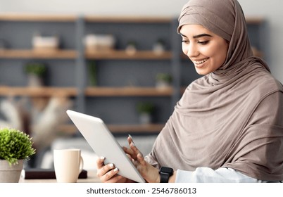 Technology. Millennial Muslim Woman Spending Time With Digital Tablet Sitting At Desk At Home Office, Reading News, Browsing Internet, Watching Videos, Checking Social Networks, Free Copy Space - Powered by Shutterstock