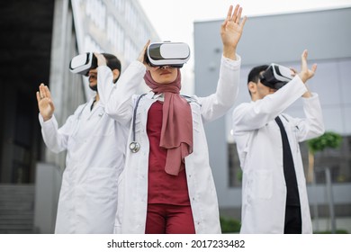Technology And Occupational Concept. Visualization Training With VR. Three Focused Asian Doctors, Wearing VR Headset, Moving Hands In The Air, Standing Outside The Modern Hospital Building