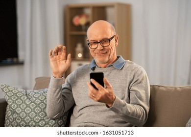 Technology, Old Age And People Concept - Happy Smiling Bald Senior Man With Smartphone Having Video Call And Waving Hand At Home In Evening