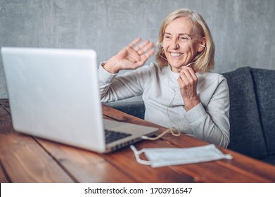 Technology, Old Age And People Concept - Happy Older Senior Woman With Face Medical Mask Working And Making A Video Call With Laptop Computer At Home During Coronavirus COVID19 Pandemic. Stay Home