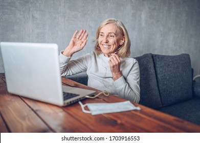 Technology, Old Age And People Concept - Happy Older Senior Woman With Face Medical Mask Working And Making A Video Call With Laptop Computer At Home During Coronavirus COVID19 Pandemic. Stay Home