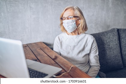 Technology, Old Age And People Concept - Lonely Sad Older Senior Woman In Face Medical Mask Working And Making A Video Call With Laptop Computer At Home During Coronavirus COVID19 Pandemic. Stay Home