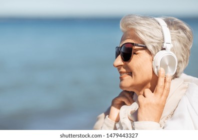 Technology, Old People And Leisure Concept - Senior Woman In Headphones And Sunglasses Listening To Music On Summer Beach In Estonia