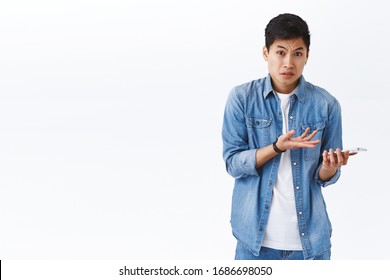 Technology, online lifestyle concept. Portrait of frustrated and displeased young complaining asian man pointing at mobile phone with dismay and puzzled expression, dont know why internet not working - Shutterstock ID 1686698050