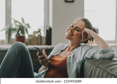 Technology in our life. Waist up portrait of happy smilng woman on sofa enjoying music with closing eyes while listening it by mobile phone via wireless earbuds