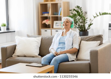 Technology, People And Lifestyle Concept - Happy Senior Woman In Headphones And Tablet Pc Computer Listening To Music At Home