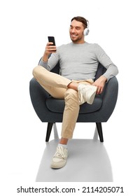 Technology, People And Music Concept - Happy Smiling Man With Smartphone And Earphones Sitting In Chair Over White Background