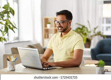technology, remote job and lifestyle concept - happy indian man in glasses with laptop computer working at home office