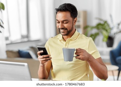 Technology, Remote Job And Lifestyle Concept - Happy Indian Man With Smartphone Drinking Coffee Or Tea At Home Office