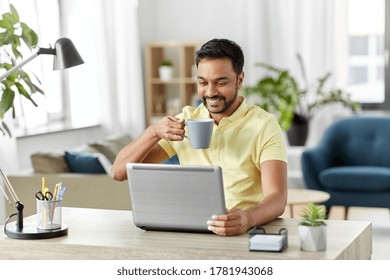 Technology, Remote Job And Lifestyle Concept - Happy Indian Man With Laptop Computer Drinking Coffee Or Tea At Home Office