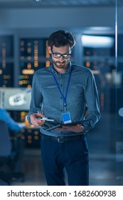 In Technology Research Facility: Chief Engineer Stands In The Middle Of The Lab And Uses Tablet Computer. Team Of Industrial Engineers, Developers Work On Engine Design Use Digital Whiteboard And PC