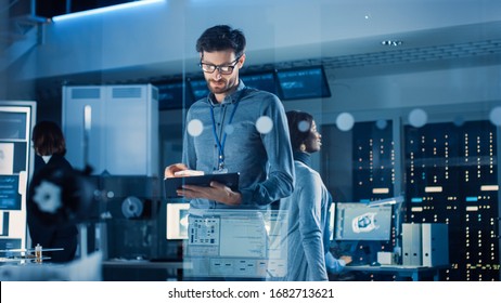 In Technology Research Facility: Chief Engineer Stands In Middle Of The Lab And Uses Tablet Computer. Team Of Industrial Engineers, Developers Work On Engine Design Use Digital Whiteboard And Computer