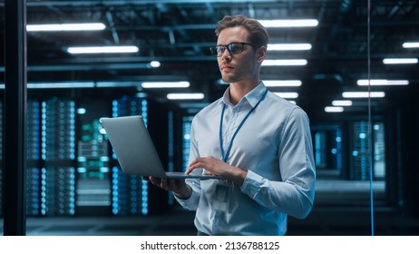 In Technology Research Facility: Chief Engineer Stands In The Middle Of The Lab And Uses Laptop Computer. E-Business Digital Entrepreneur Examining Cloud Web Services At The Evening