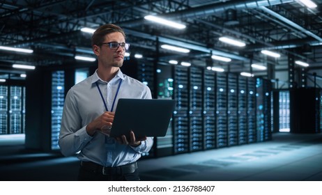 Technology Research Facility: Male Project Manager Standing At The Corridor And Uses Tablet Computer. Engineers Or Developers Work On Engine Design And Use Digital Computers