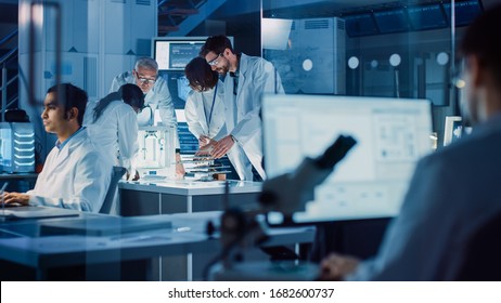 In Technology Research Laboratory: Diverse Team of Industrial Scientists, Engineers, Developers Gather Around Illuminated Table and Inspect Blueprints, Adjust 3D Printer, Choose Component Motherboard