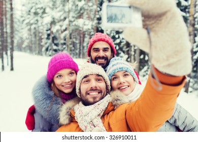 Technology, Season, Friendship And People Concept - Group Of Smiling Men And Women Taking Selfie With Digital Camera In Winter Forest