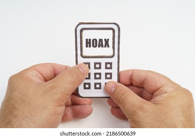 Technology and security concept. On a white background, in the hands of a person, a cardboard model of a telephone with an inscription on the screen - HOAX