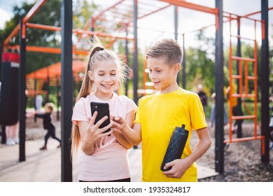 Technology and sport for children. Two teenage kids using smartphone and online workout app. Twins boy and girl watching video on phone during break from sports lesson at school at outside gym. - Powered by Shutterstock