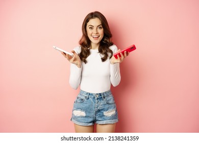 Technology, Spring Promo Concept. Stylish Glamour Woman Holding Two Smartphones, Mobile Phones In Both Hands, Smiling Pleased, Buying New Cellphone, Pink Background