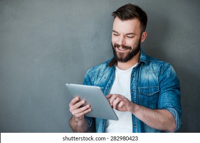 Technology takes you to the top. Happy young man holding digital tablet and smiling while standing against grey background