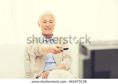 technology, television, age and people concept - happy senior woman watching tv and changing channel with remote control at home