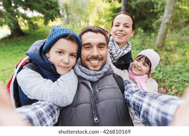 Technology, Travel, Tourism, Hike And People Concept - Happy Family With Backpacks Taking Selfie And Hiking